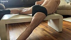 The bodybuilder lies on the desk for an aggressive myofascial pressure and release stretching session in underwear using a percussion massager