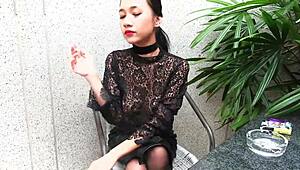 Young girl in leather skirt lights up topless outdoors.